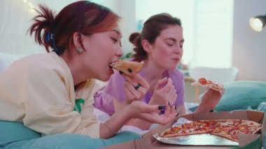 Pijama partisinde yatakta pizza yiyip konuşan çok uluslu tatlı kızlar.