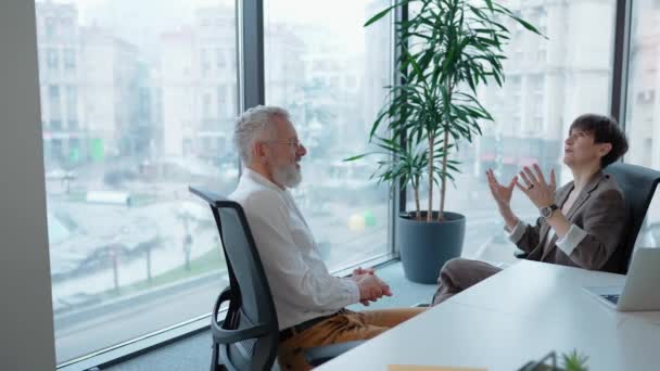 オフィスミーティングで彼の女性の同僚と話す幸せな成熟した灰色の髪の男 — ストック動画