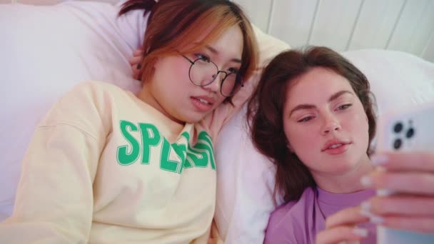 Дві Багатокультурні Чарівні Жінки Друзі Дивляться Мобільний Телефон Розмовляють Ліжку — стокове відео