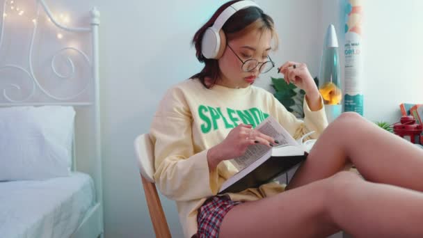 Pensiv Ung Asiatisk Kvinna Glasögon Lyssna Musik Hörlurar Och Läsa — Stockvideo