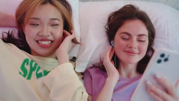 Çok Kültürlü Komik Kızların Kulaklıkla Müzik Dinledikleri Yatıya Kaldıkları Yatakta — Stok video