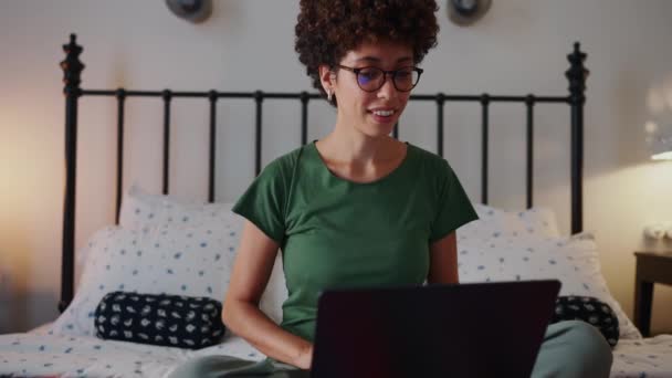 笑顔のアフリカの女性 メガネとカーリーヘア 自宅からベッドのラップトップで作業 — ストック動画