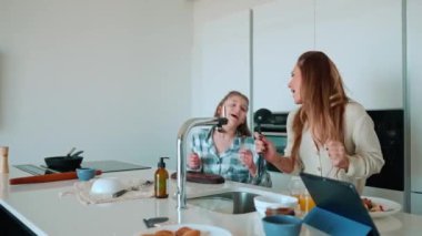 Komik anne ve kız mutfakta dans edip şarkı söylüyorlar.
