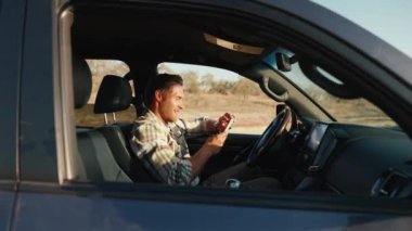 Yazın araba kullanırken telefonda mesajlaşan güneşli sarışın adam.