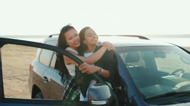 Gülen çok kültürlü kızlar yazın kumların üzerinde arabanın yanında poz veriyor ve sarılıyorlar.