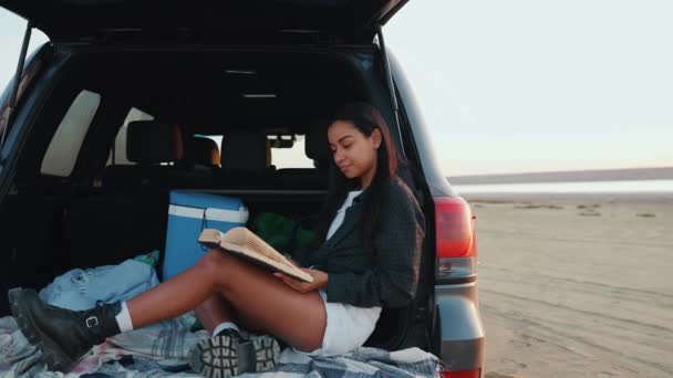 Zrelaksowana Afrykańska Kobieta Czyta Książkę Bagażniku Samochodu Pobliżu Ujścia Rzeki — Wideo stockowe