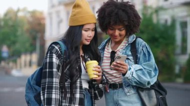 Sırt çantalı, cep telefonuna bakan ve sokakta konuşan çok kültürlü kız öğrencilere gülüyorlar.