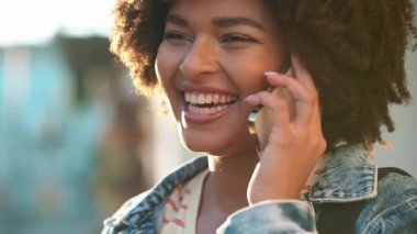 Gülen kıvırcık saçlı Afrikalı kadın dışarıda cep telefonuyla konuşuyor.