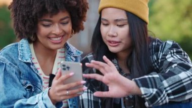 Mutlu çok kültürlü bayan arkadaşlar konuşuyor ve sonbaharda sokakta telefona bakıyorlar.