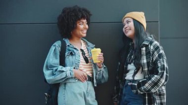 Çok kültürlü, çok kültürlü, kahve içen ve dışarıda siyah duvarın yanında konuşan hoş bayan arkadaşlar.