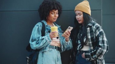 Cep telefonuyla mesajlaşan ve dışarıdaki siyah duvarın yanında konuşan çok kültürlü bayan arkadaşlar.