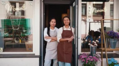 Smiling multicultural waitresses in aprons welcoming guests at door of cafe