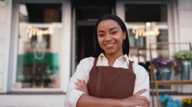 Cute african waitress in apron looking at camera and welcoming guests at door of cafe
