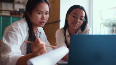 Charming multinational waitresses working on laptop and filling out reports sitting in cafe