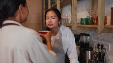 Back view of funny multicultural waitresses smelling coffee in cup at cafe