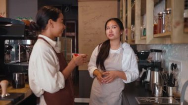 Side view of confident multicultural waitresses talking and drinking at cafe