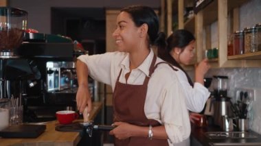 Side view of cheerful multicultural waitresses brewing coffee at cafe