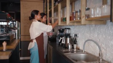 Side view of concentrated multicultural waitresses setting out cups behind counter at cafe
