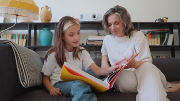 自宅のソファーで彼女の灰色の髪の若いママと本を読む自信のある少女 — ストック動画
