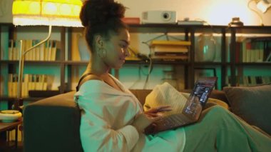 Akşam evde dizüstü bilgisayar seyreden Afro-Afrikalı bir kadının yan görüntüsü