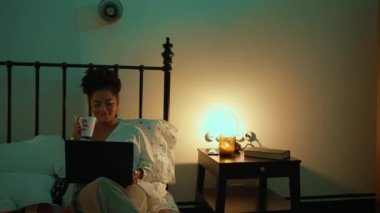 Çekici bir kadın laptopta mesaj atıyor ve akşamları yatakta çay içerken şarkı söylüyor.