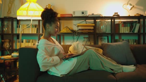 ラップトップで作業し 夕方自宅のソファーに座って話している美しいアフリカの女性 — ストック動画