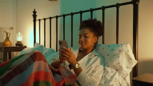 Позитивная Африканская Женщина Пишет Смс Мобильный Телефон Кровати Дома Вечером — стоковое видео