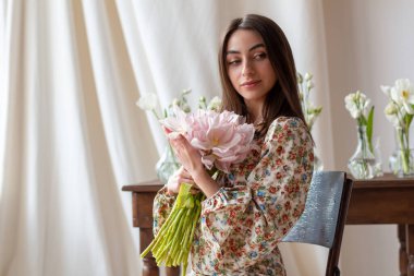 Çiçekli, siyah saçlı, aydınlık odada bir buket lale taşıyan güzel bir kadın.