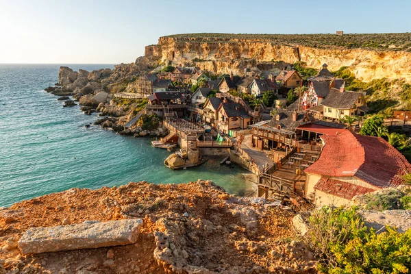 Malta, Il-Mellieha. Anchor Bay 'deki ünlü Temel Reis Köyü manzarası. Turkuaz deniz suları, mavi gökyüzü ve kayalıklarda gün batımı ışığı..