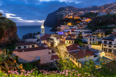 Akşam karanlığında Camara de Lobos 'un şehir manzarası Portekiz' in Madeira adasındaki sahil kasabasının mimarisini aydınlattı.