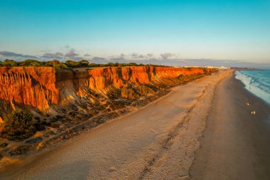 Algarve, Portekiz kıyı şeridi, kumlu sahil, Atlantik Okyanusu dalgaları ve gün batımında kızıl kayalıklar. Hava aracı görünümü.