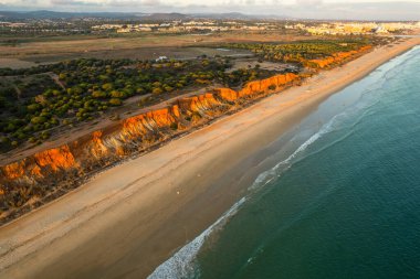 Algarve, Portekiz kıyı şeridi, kumlu sahil, Atlantik Okyanusu dalgaları ve gün batımında kızıl kayalıklar. Hava aracı görünümü.