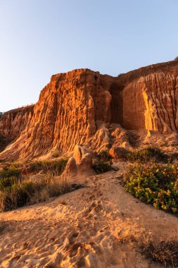 Algrave, Portekiz 'deki kumlu sahilde gün batımında kızıl kayalıklar