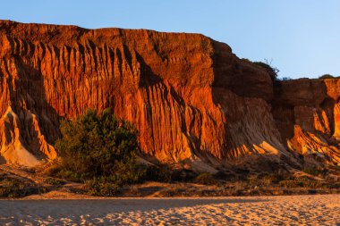 Algrave, Portekiz 'deki kumlu sahilde gün batımında kızıl kayalıklar