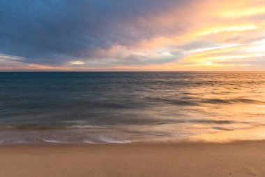 Okyanus dalgaları ve renkli gökyüzü ve bulutlarla kumlu sahilde gün batımı, Algarve, Portekiz