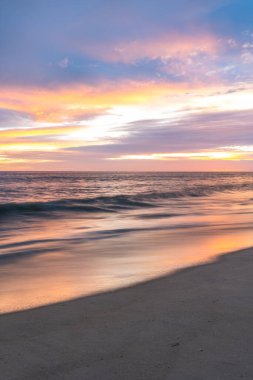 Okyanus dalgaları ve renkli gökyüzü ve bulutlarla kumlu sahilde gün batımı, Algarve, Portekiz