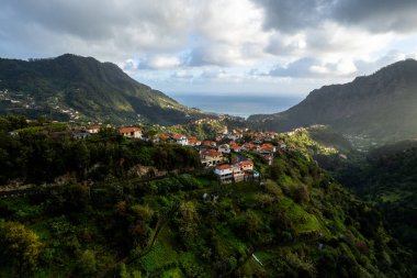 Madeira Adası manzarası, tepelerdeki küçük köy ve yeşil yemyeşil orman. Hava aracı görüntüsü. Portekiz seyahati.