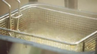 Metal bir sepet ile kaynamış yağda kızartılan sokak yemeği balıklarının yakın çekim görüntüleri. Çıtır çıtır yüzey şekillendikçe sıcak kabarcıklar yükselir. Cızırtılı sesi ve altın dokuları olan otantik şehir yemekleri sahnesi.