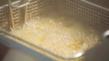 Metal bir sepet ile kaynamış yağda kızartılan sokak yemeği balıklarının yakın çekim görüntüleri. Çıtır çıtır yüzey şekillendikçe sıcak kabarcıklar yükselir. Cızırtılı sesi ve altın dokuları olan otantik şehir yemekleri sahnesi.