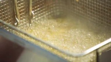 Metal bir sepet ile kaynamış yağda kızartılan sokak yemeği balıklarının yakın çekim görüntüleri. Çıtır çıtır yüzey şekillendikçe sıcak kabarcıklar yükselir. Cızırtılı sesi ve altın dokuları olan otantik şehir yemekleri sahnesi.