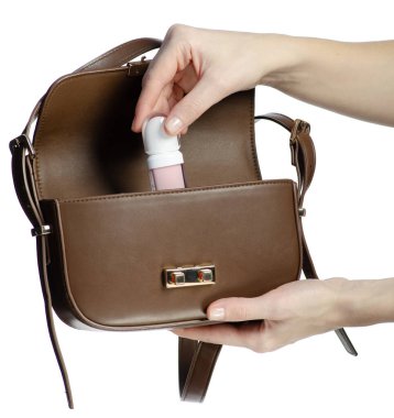 El beyaz arka planda kahverengi çantaya dudak parlatıcısı koyar.