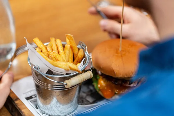 fast food and people concept - close up of man with fork and knife eating burger and french fries at restaurant