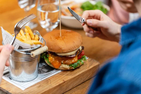 Stock image fast food and people concept - close up of man with fork and knife eating burger and french fries at restaurant