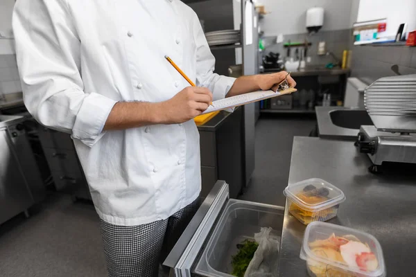 餐饮业 职业和人的概念 关闭男性厨师 在厨房冰箱中做剪贴板盘点 — 图库照片
