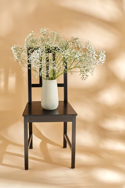 home decor and design concept - close up of gypsophila flowers in vase on vintage chair over beige background