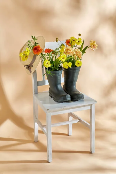 国际妇女日和花卉设计概念 米色背景的老式椅子上的橡胶靴和草帽花 — 图库照片