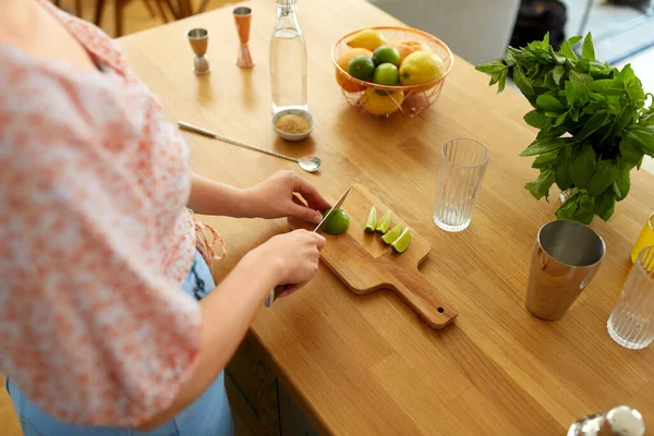 飲み物と人々のコンセプト ナイフでライムを切断し 自宅のキッチンでカクテルを作る女性のクローズアップ — ストック写真