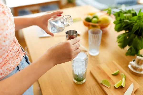飲み物と人々のコンセプト 家庭のキッチンでガラス瓶から水を注ぐ女性の閉じるとリムモヒートカクテルを作る — ストック写真