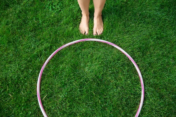 sport, leisure and fitness stuff concept - close up of hula hoop and womans feet on grass