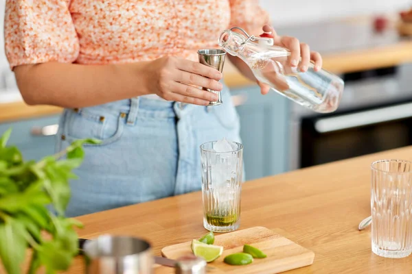 飲み物と人々のコンセプト 家庭のキッチンでガラス瓶から水を注ぐ女性の閉じるとリムモヒートカクテルを作る — ストック写真